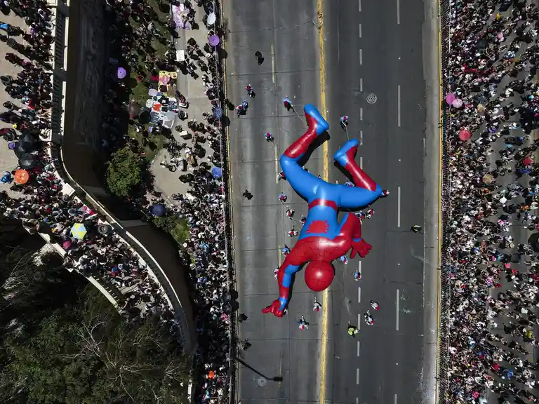 An aerial view shows a large, red-and-blue Spider-Man balloon lying upside down in the middle of a street during a parade…