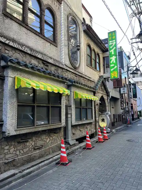 A street view of a Japanese building with stone-textured walls, arched windows, and green-and-yellow striped awnings…