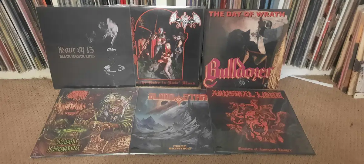 Six black metal album covers are displayed on a carpeted floor, with a bookshelf in the background. The albums are 'Hour Of…