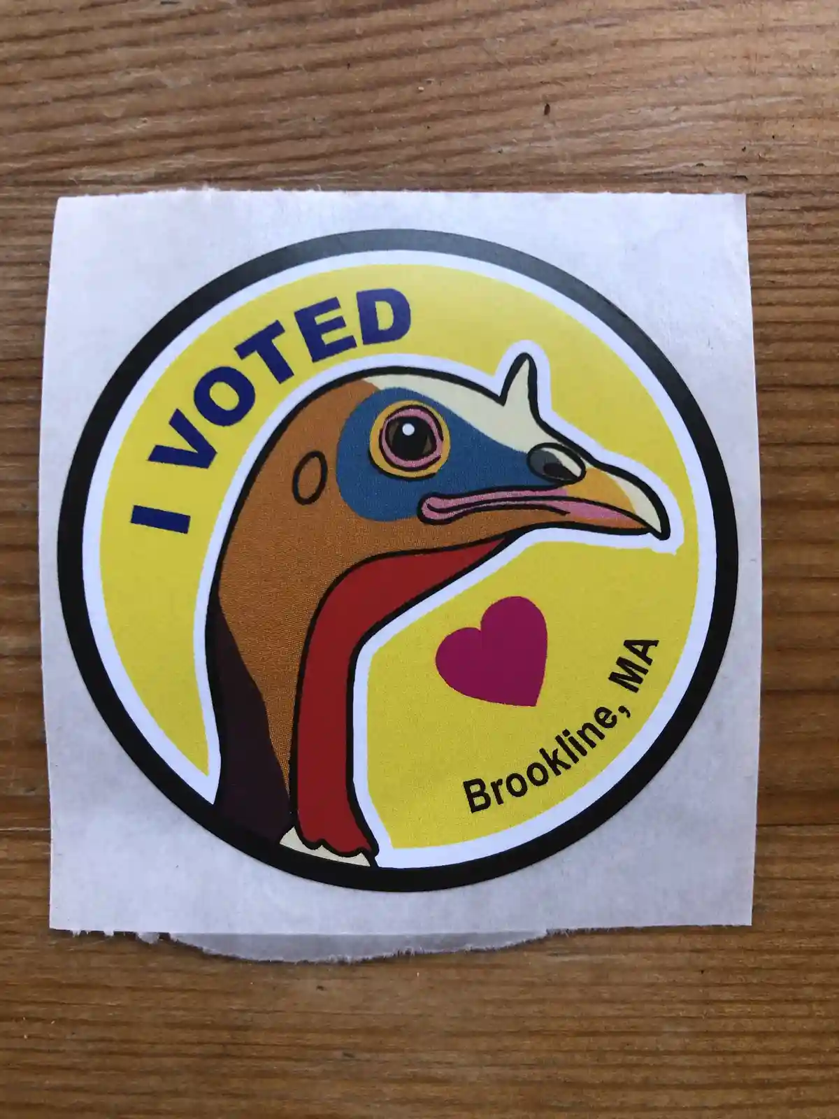 A circular 'I VOTED' sticker featuring a cartoon turkey with a red wattle and blue face, set against a yellow background…