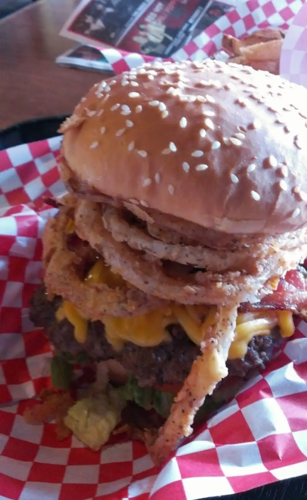 A towering, messy burger with multiple beef patties, melted cheese, crispy bacon, and a thick stack of fried onion rings…