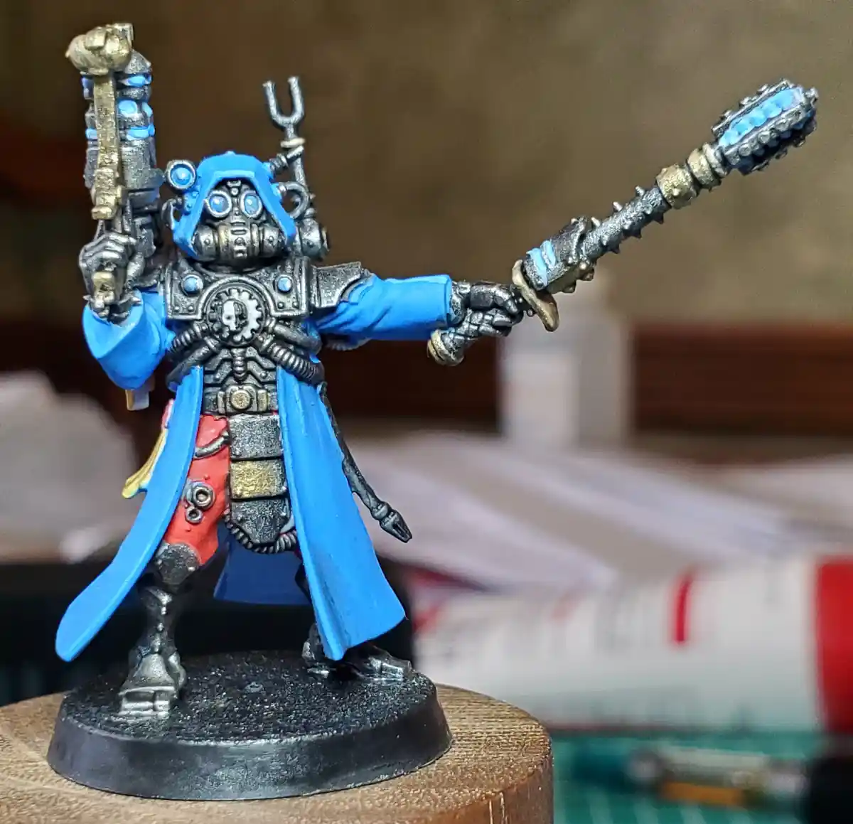 A painted miniature figure of a heavily armored, blue-clad sci-fi warrior with a gas mask, holding a large hammer and a…