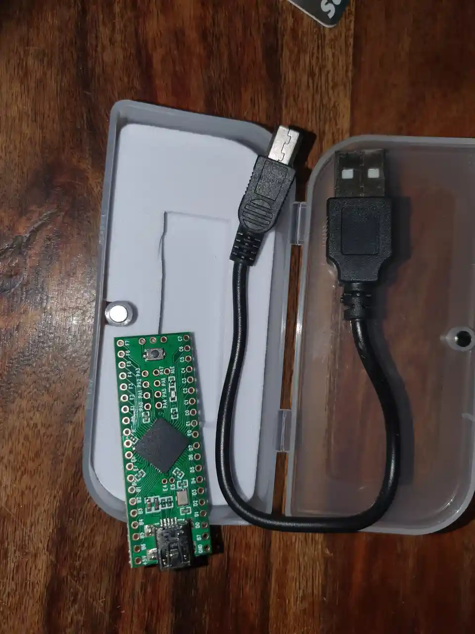An overhead shot shows a small green microcontroller board with a micro-USB port, a standard USB-A plug, and a short black…
