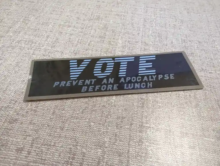 A rectangular sticker with a dark background and light blue striped text lies on a textured beige fabric surface. The text…