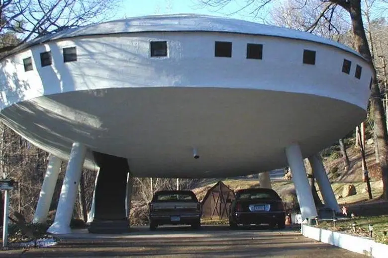 a large, white, saucer-shaped building with small square windows and thick pillars supporting its underside, parked in a…