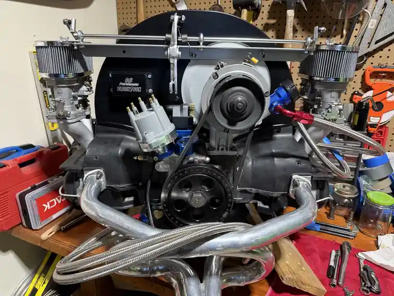 A highly modified, custom-built engine sits on a workbench in a garage, featuring chrome air filters, a 'CB Performance…