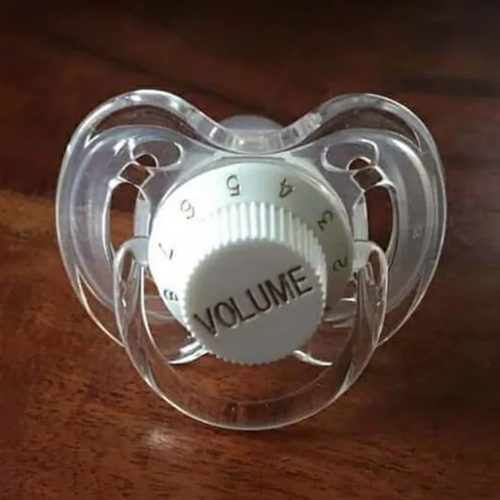 A clear plastic pacifier with a white, circular dial in the center labeled 'VOLUME' and numbered 0 through 6, resting on a…