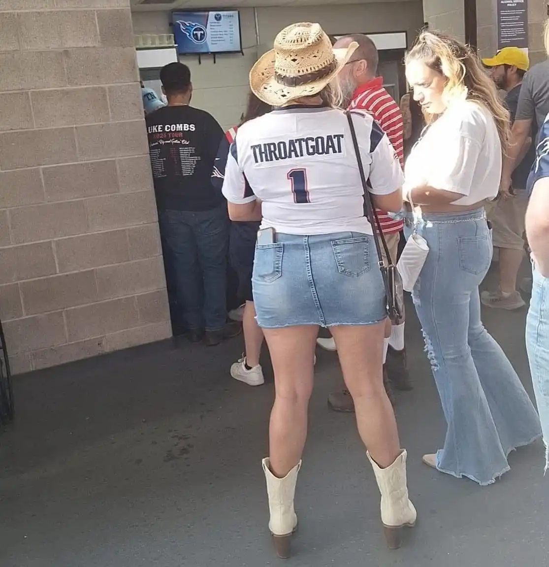 A woman viewed from behind wears a white Tennessee Titans jersey with 'THROATGOAT' and the number '1' printed on the back…