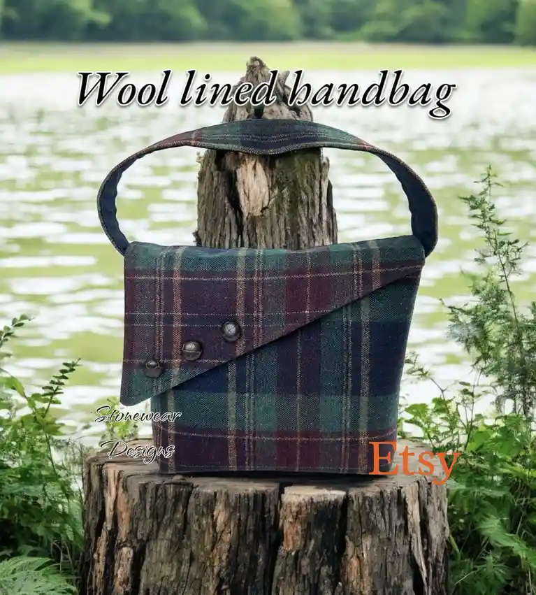 A plaid wool-lined handbag with a flap closure and three buttons sits on a tree stump by a body of water, with text overlay…