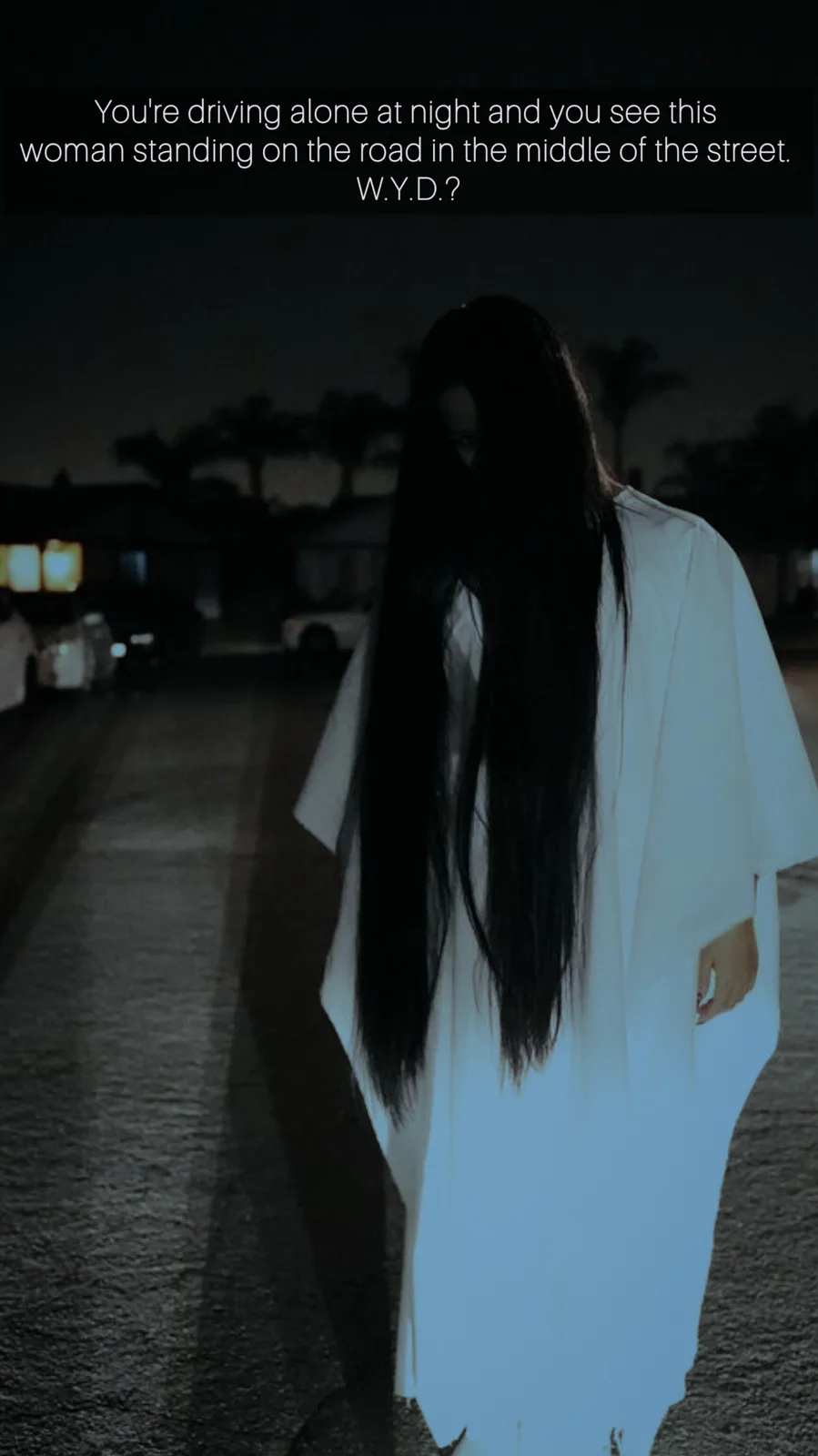 A dark, atmospheric night photo shows a woman from behind, wearing a long white robe and obscuring her face with long black…
