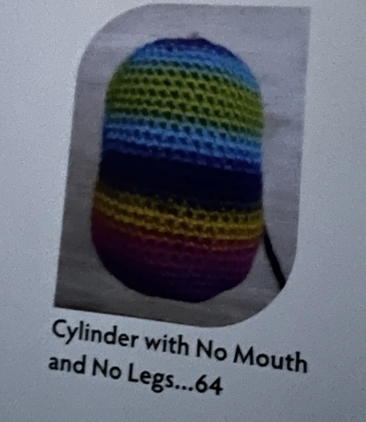 A rainbow-colored, crocheted cylindrical object, resembling a backpack or pouch, is shown against a plain background. The…