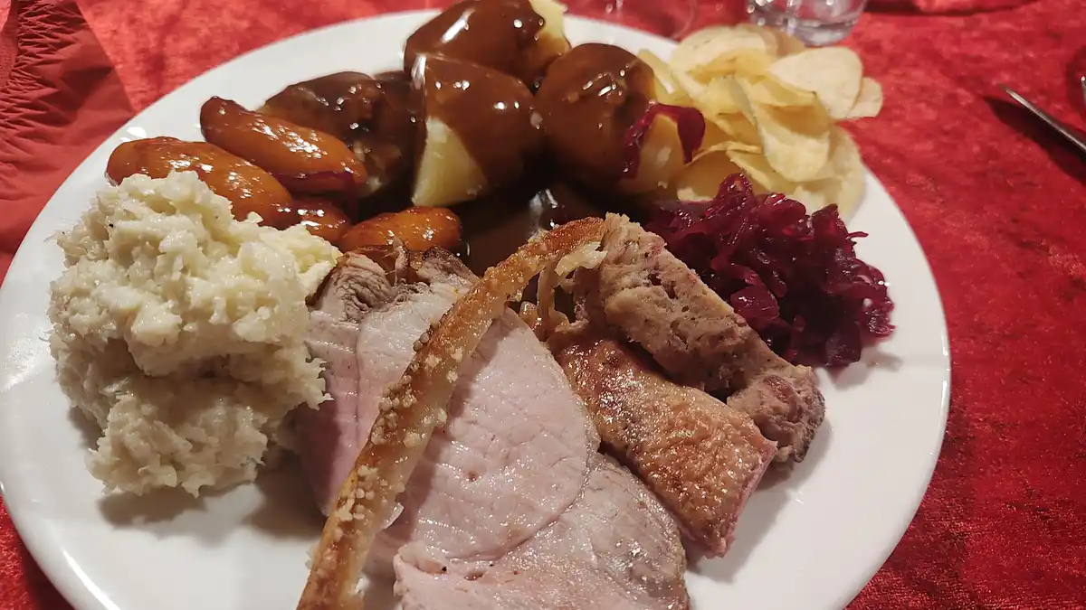 A plate of traditional holiday food including sliced pork, mashed potatoes, sauerkraut, potato dumplings with gravy, and…