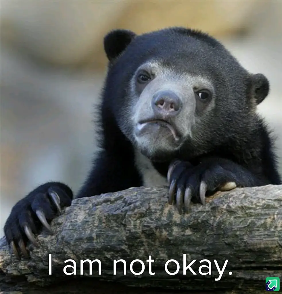 A close-up photo of a sad-looking spectacled bear with a downturned mouth and droopy eyes, resting its paws on a log. The…