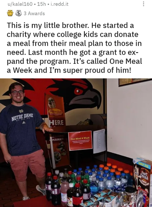 A smiling young man in a Notre Dame t-shirt stands beside a table piled with donated food items including soda bottles…