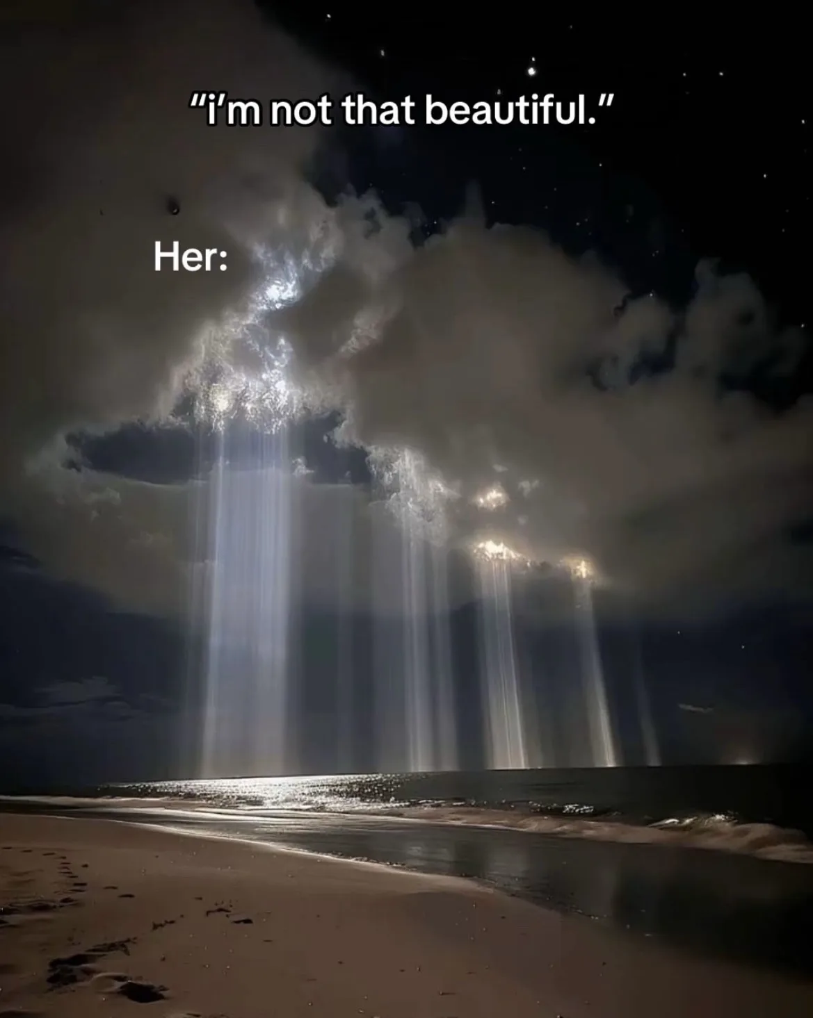 A night beach scene with dramatic beams of light piercing through clouds over the ocean, visually representing a person's…