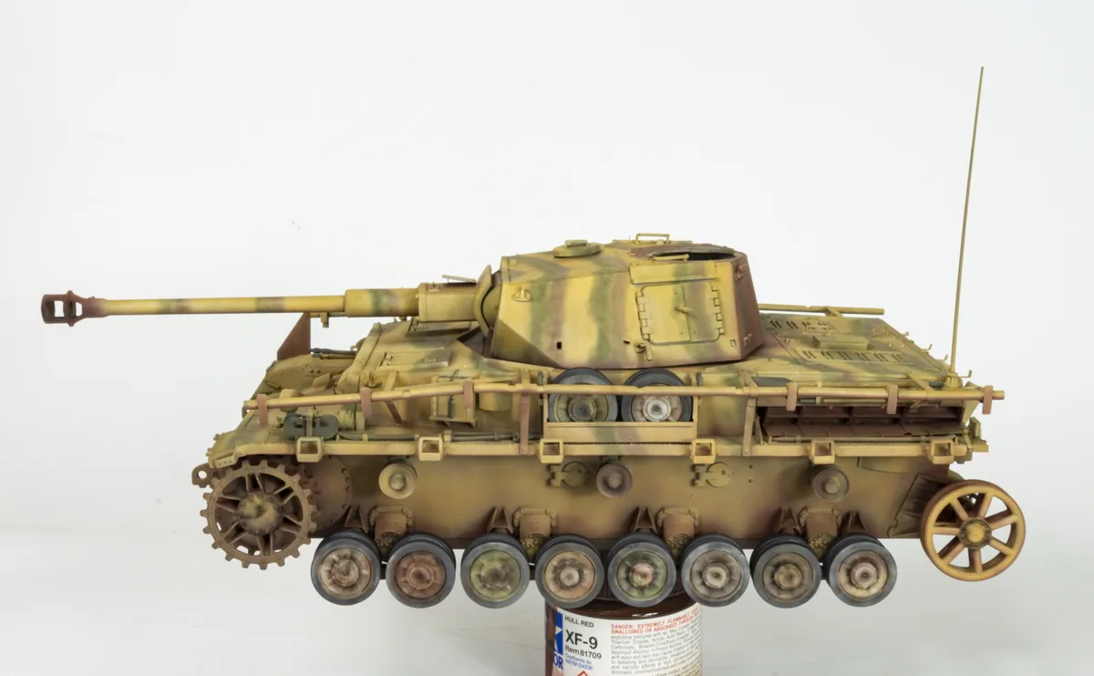 A detailed scale model of a German tank, painted in a desert camouflage pattern, is displayed against a plain white…