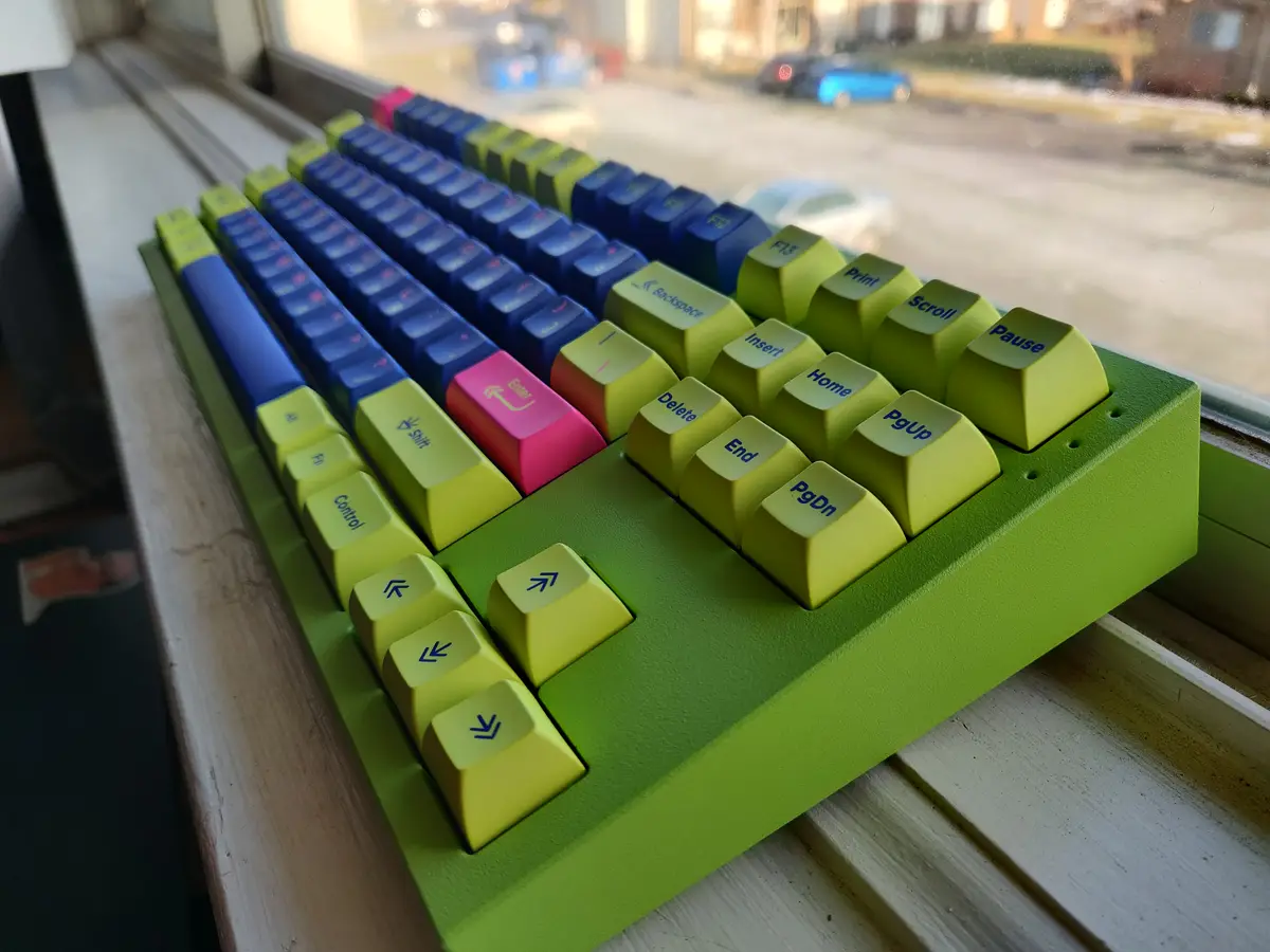 A close-up photo of a custom mechanical keyboard with a bright green case, lime green keys, blue keys, and a pink enter key…