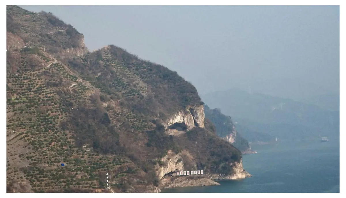 A scenic mountainous coastline with a steep cliffside covered in sparse vegetation, overlooking a large body of water. At…