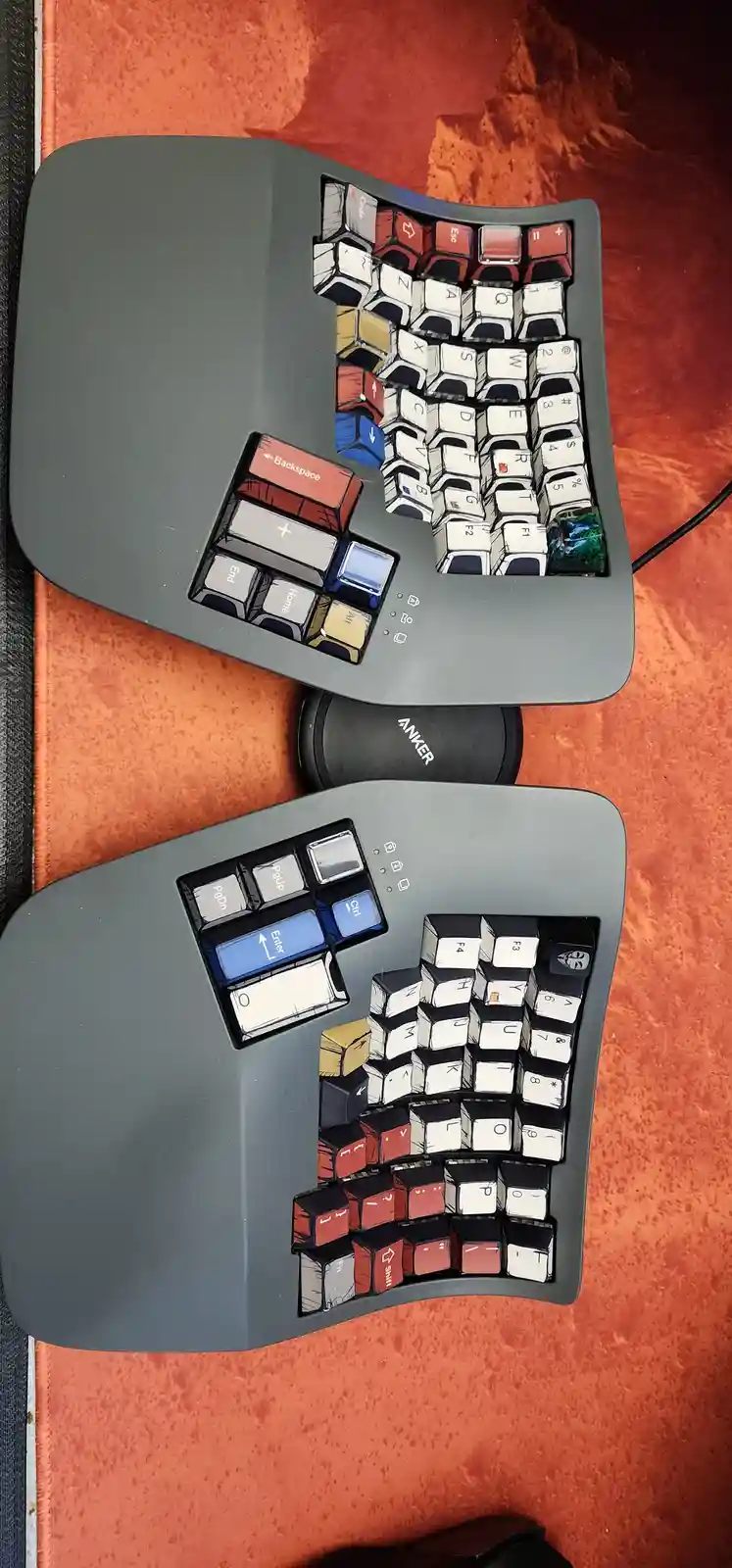Two ergonomic split keyboards are shown from above on an orange textured surface, their keycaps replaced with cartoonish…