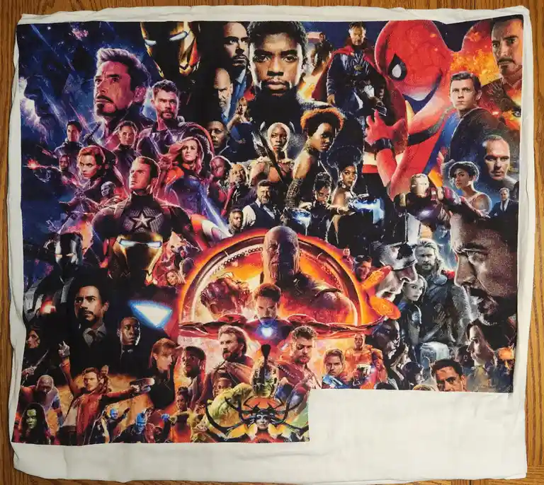 A white towel laid flat on a wooden surface displays a colorful, dense collage of characters from the Marvel Cinematic…