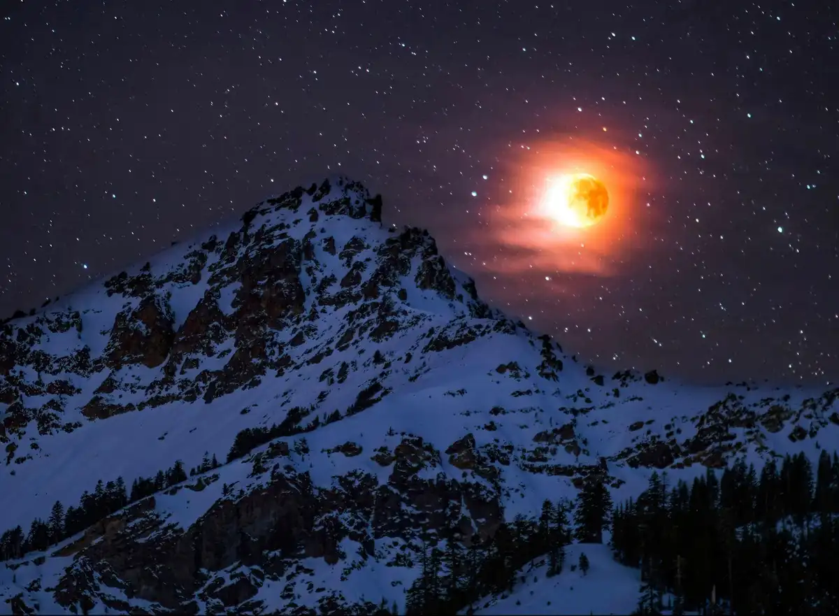 A snowy mountain peak under a starry night sky, with a large, glowing orange moon partially obscured by clouds. The overlaid…