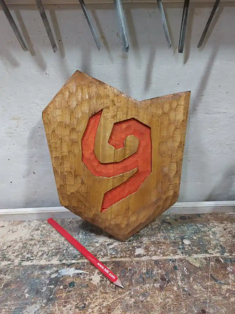 A hand-carved wooden sign shaped like a shield features a 3D carved red logo resembling the Dota 2 game emblem. The carving…