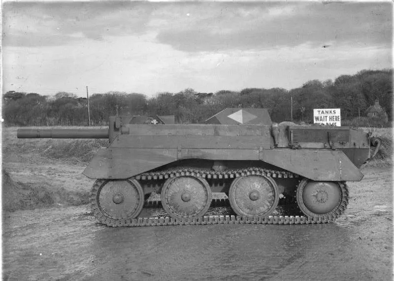 A black-and-white photo shows a military tank with a sign attached to its rear that reads 'TANKS WAIT HERE'. The tank is…