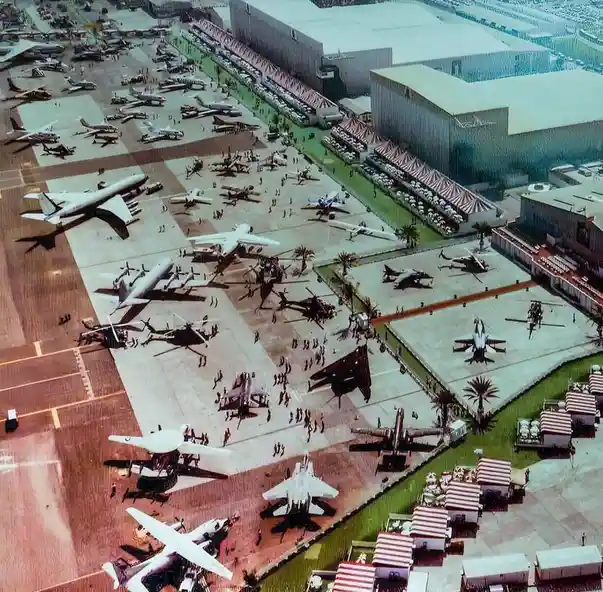 An aerial view of a massive airshow or aviation exhibition with dozens of different aircraft, including jets, prop planes…