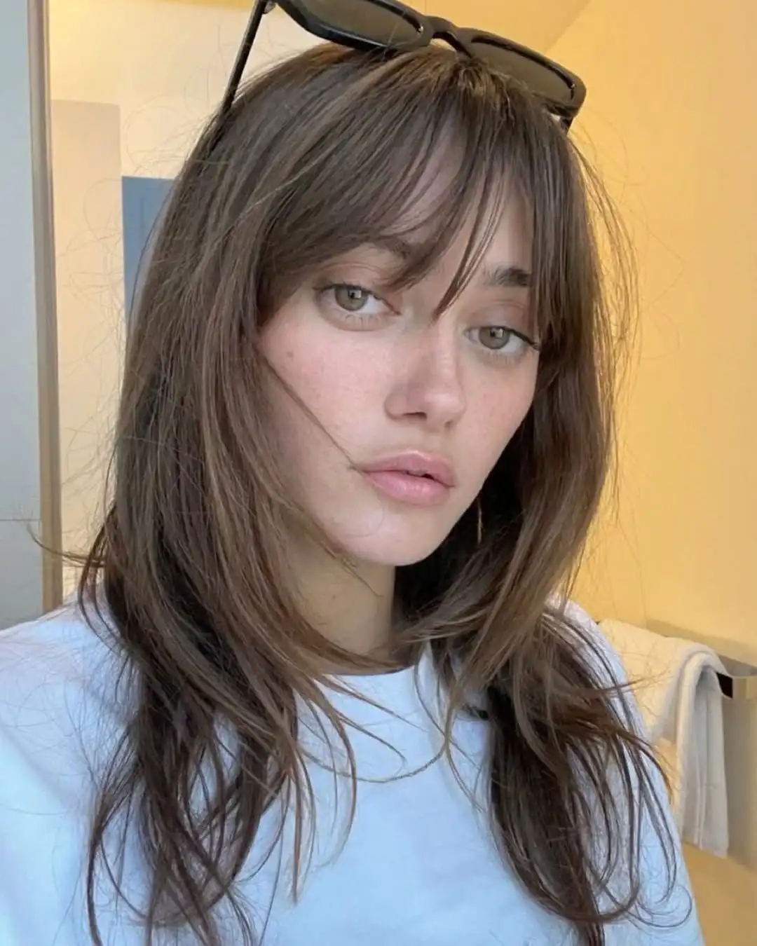 A woman with brown hair and sunglasses perched on her head looks directly at the camera with a tired, unimpressed…