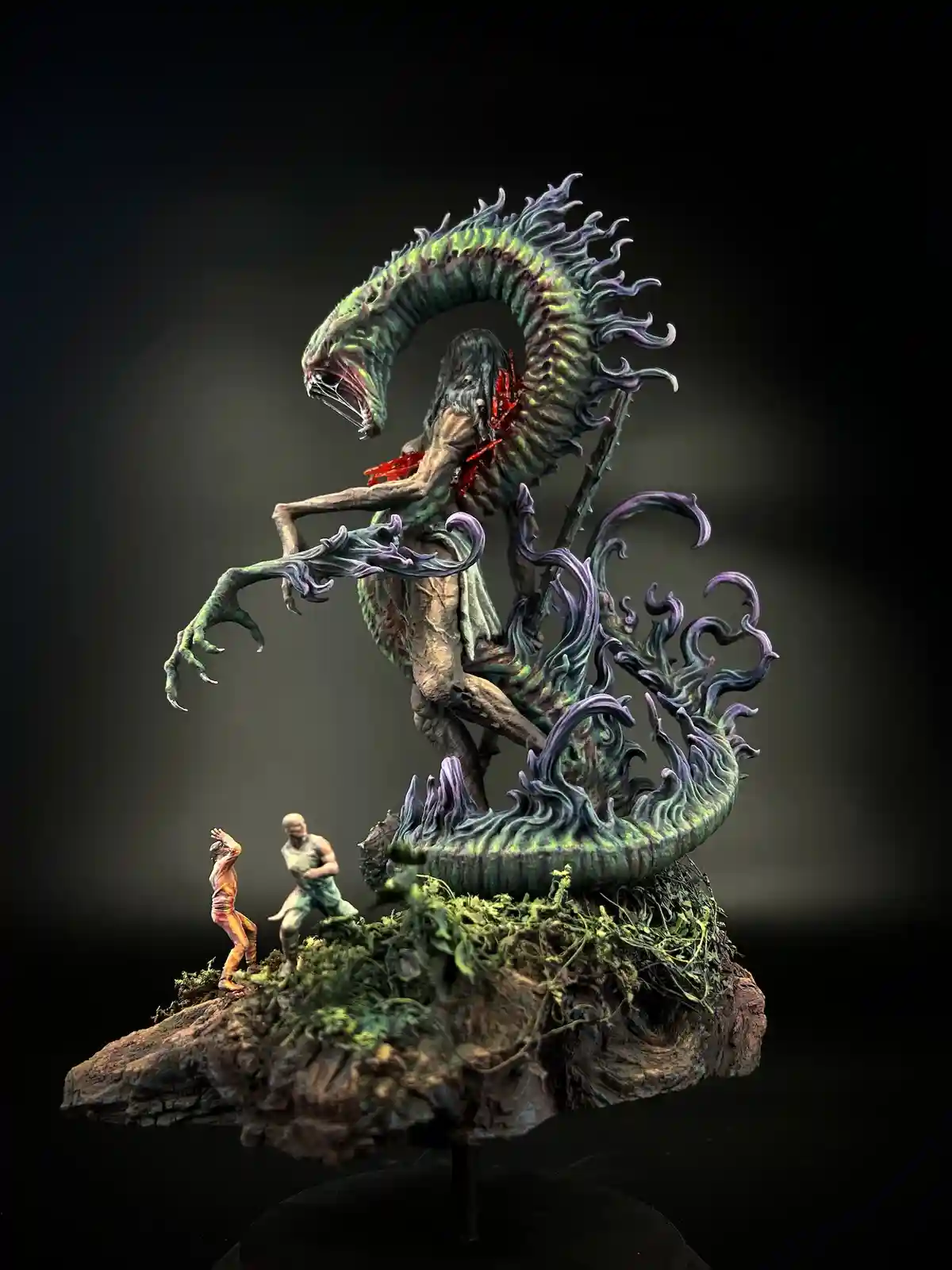 A detailed miniature sculpture depicts a monstrous, serpentine creature with a human-like upper body, its mouth agape and…