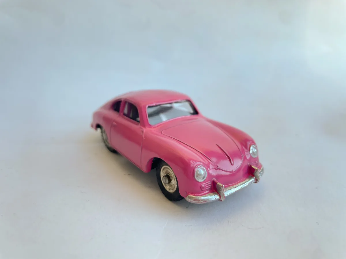 A small, pink toy car with silver trim and black wheels is photographed on a plain white surface. The car has a vintage…