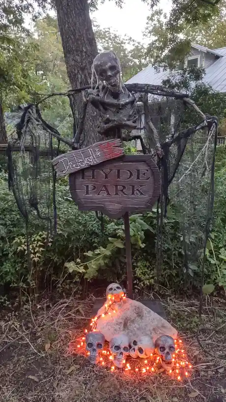 A spooky Halloween decoration features a skeletal figure draped in black netting holding a wooden sign that reads 'Dr…
