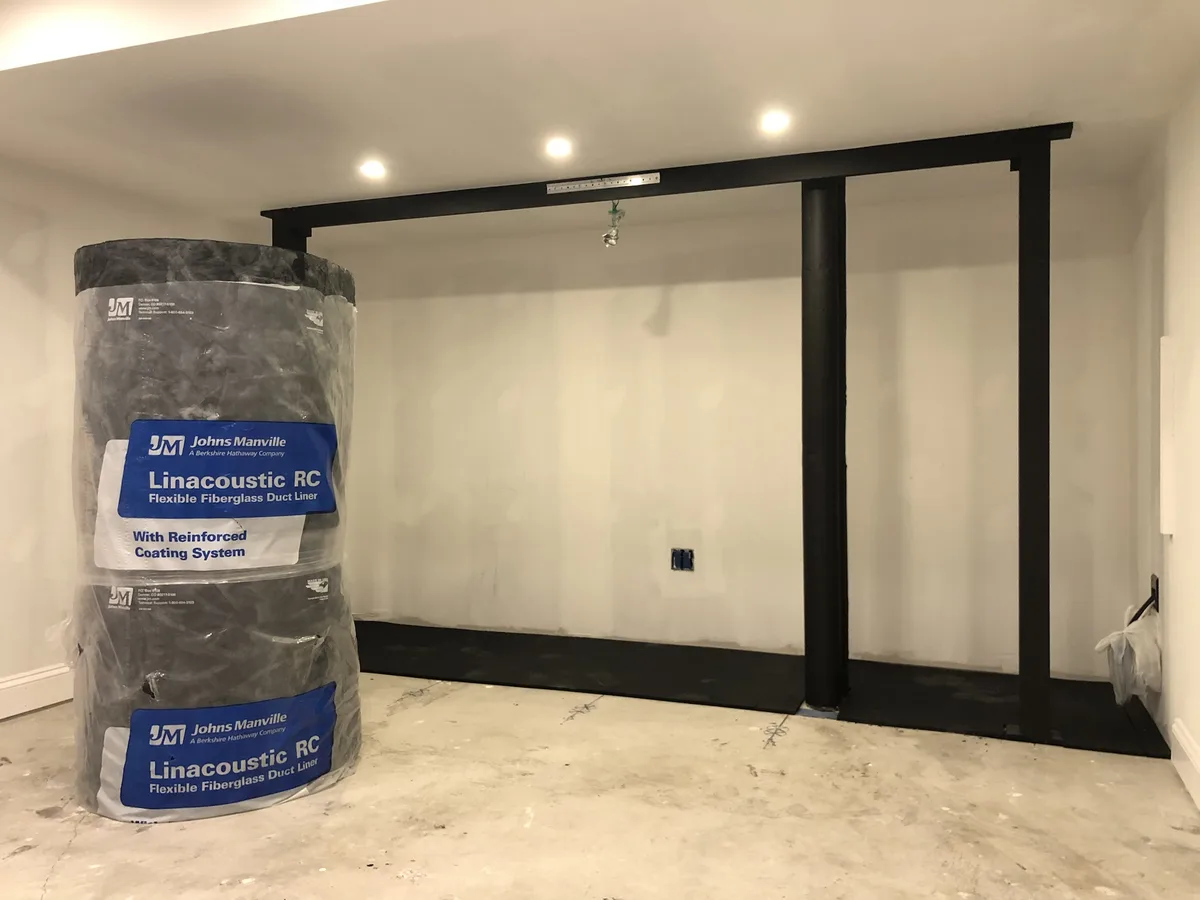 A large, wrapped roll of Johns Manville Linacoustic RC flexible fiberglass duct liner sits on a concrete floor in an…