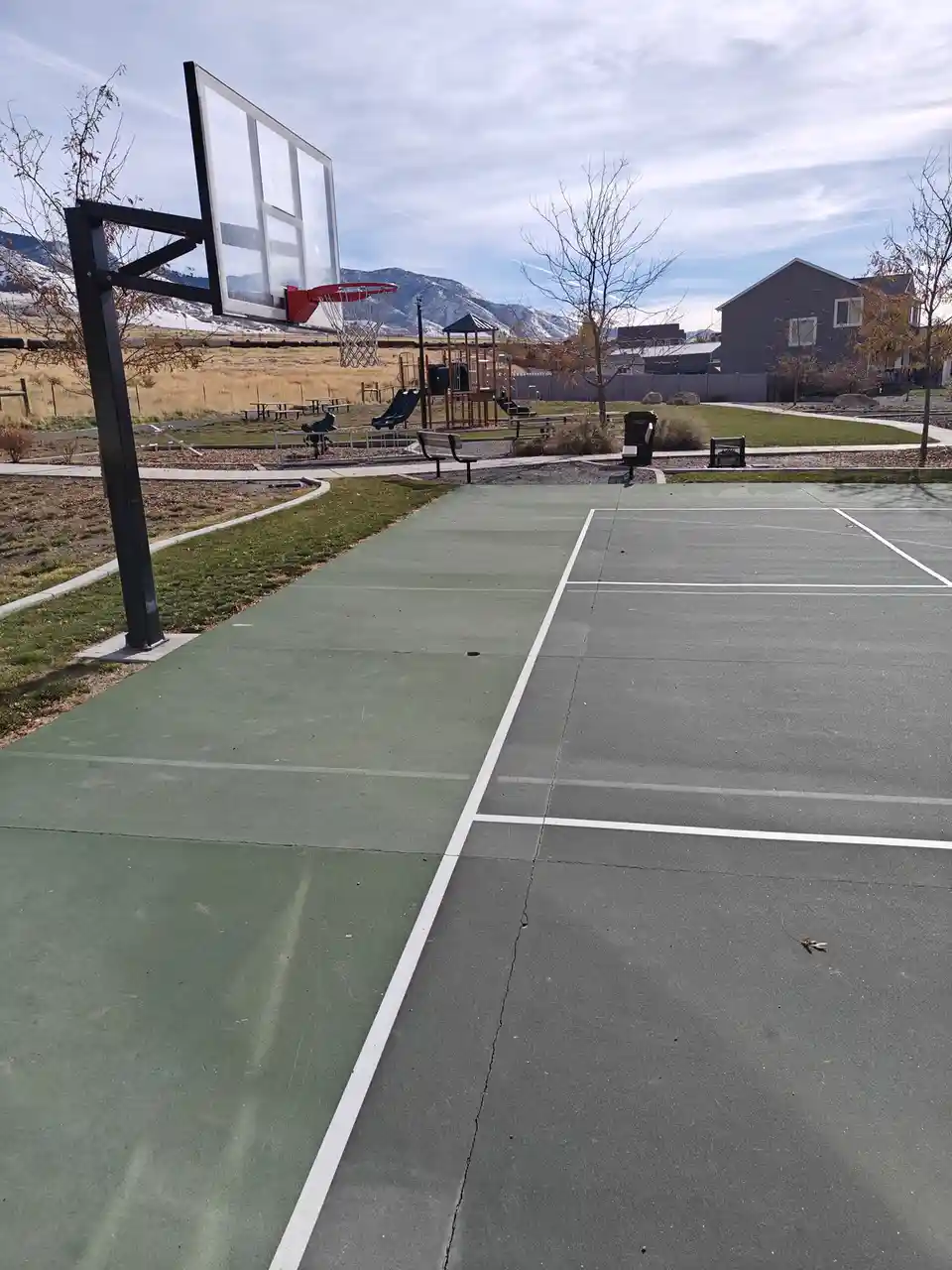 An outdoor basketball court with white lines painted on the surface, including lines that also mark a tennis court, creating…