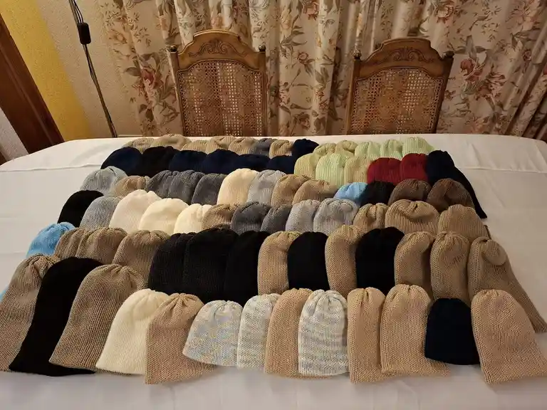 A large collection of approximately 50 hand-knitted beanies in various colors and patterns are neatly arranged in rows on a…