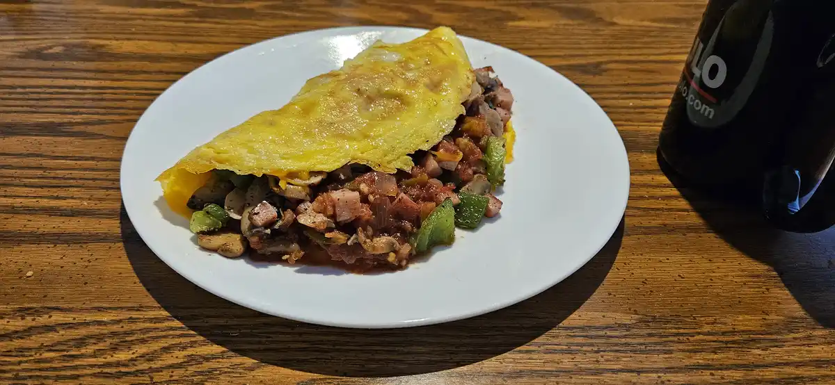 A close-up photo shows a folded, golden-yellow omelette filled with visible chunks of ham, green bell peppers, and…