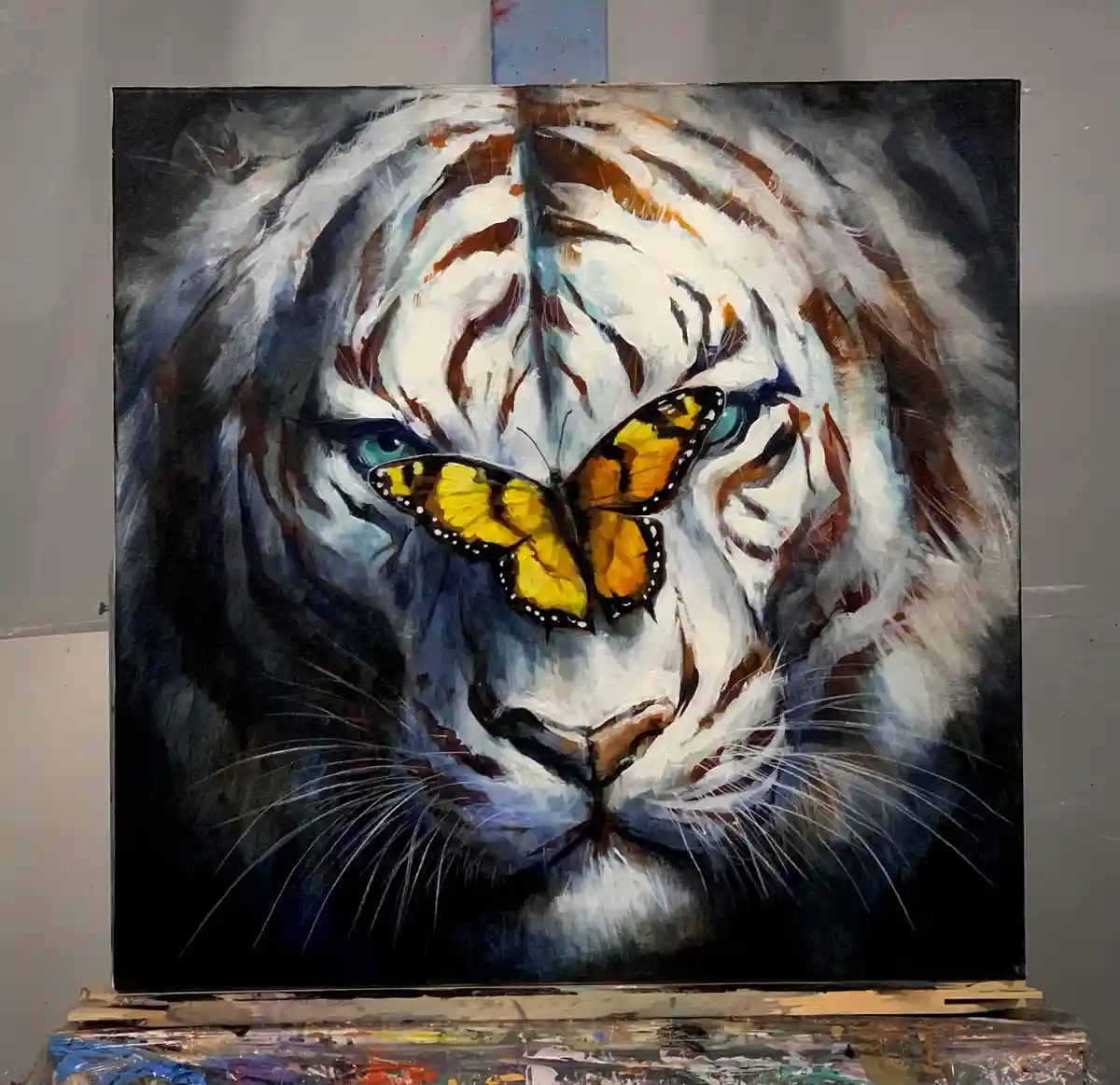 A painting of a white tiger's face with intense blue eyes, featuring a bright yellow and black butterfly resting on its…