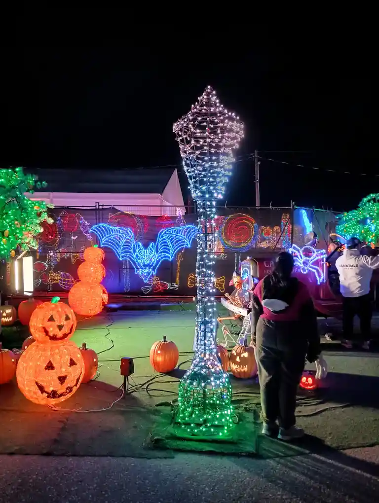 A nighttime photo of a Halloween light display featuring glowing jack-o'-lanterns, a large illuminated bat, and a skeleton…