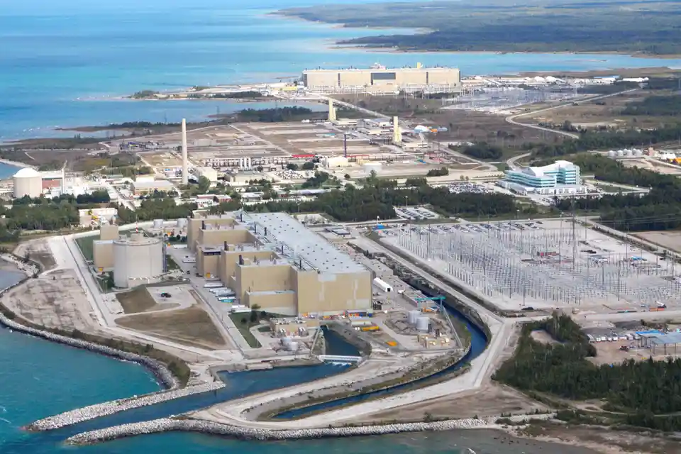 An aerial view of a large nuclear power plant complex situated on a coastline with a river channel running through it…