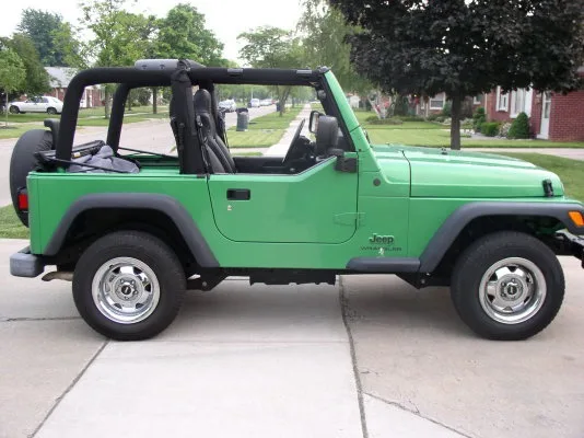A bright green Jeep Wrangler with a black soft top is parked on a concrete driveway in a suburban neighborhood. The vehicle…