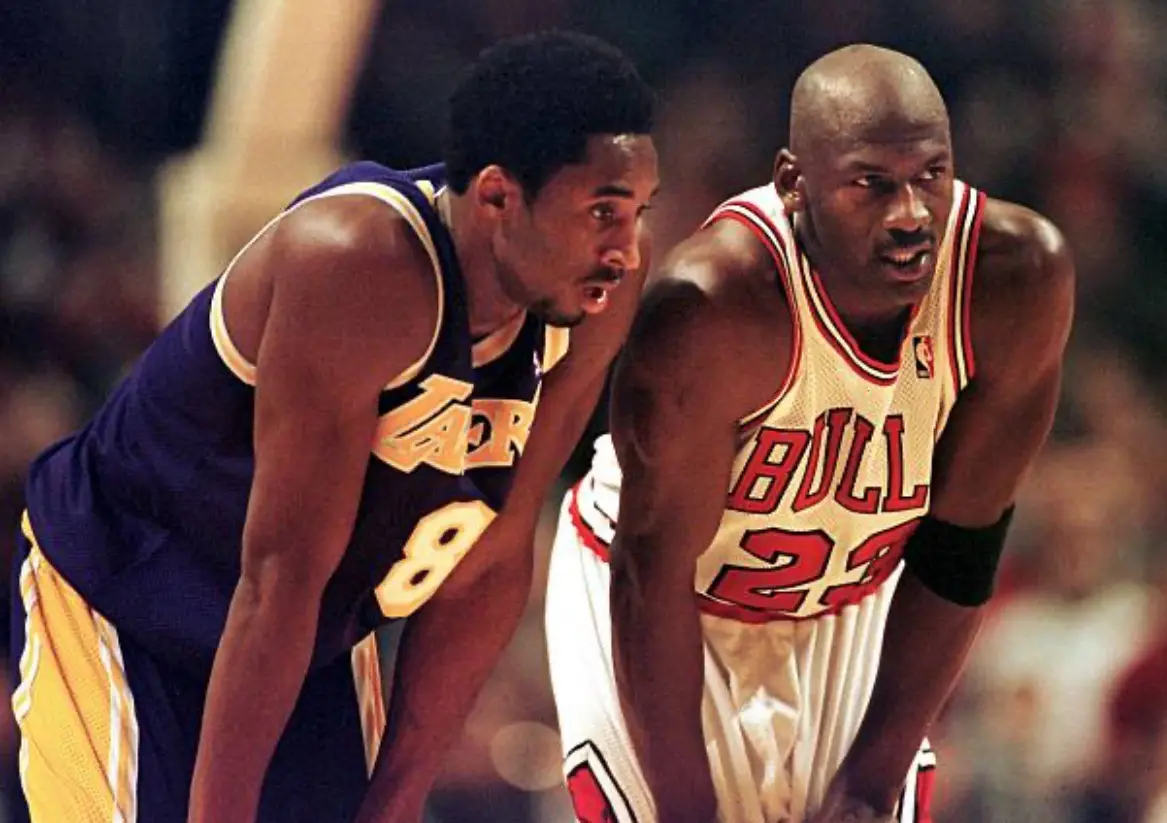 Two basketball players, Kobe Bryant in a purple and gold Lakers jersey with number 8 and Michael Jordan in a white Bulls…