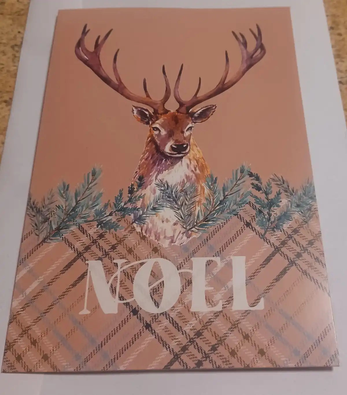 A festive Christmas card features a watercolor illustration of a stag with large antlers, framed by pine branches, set…