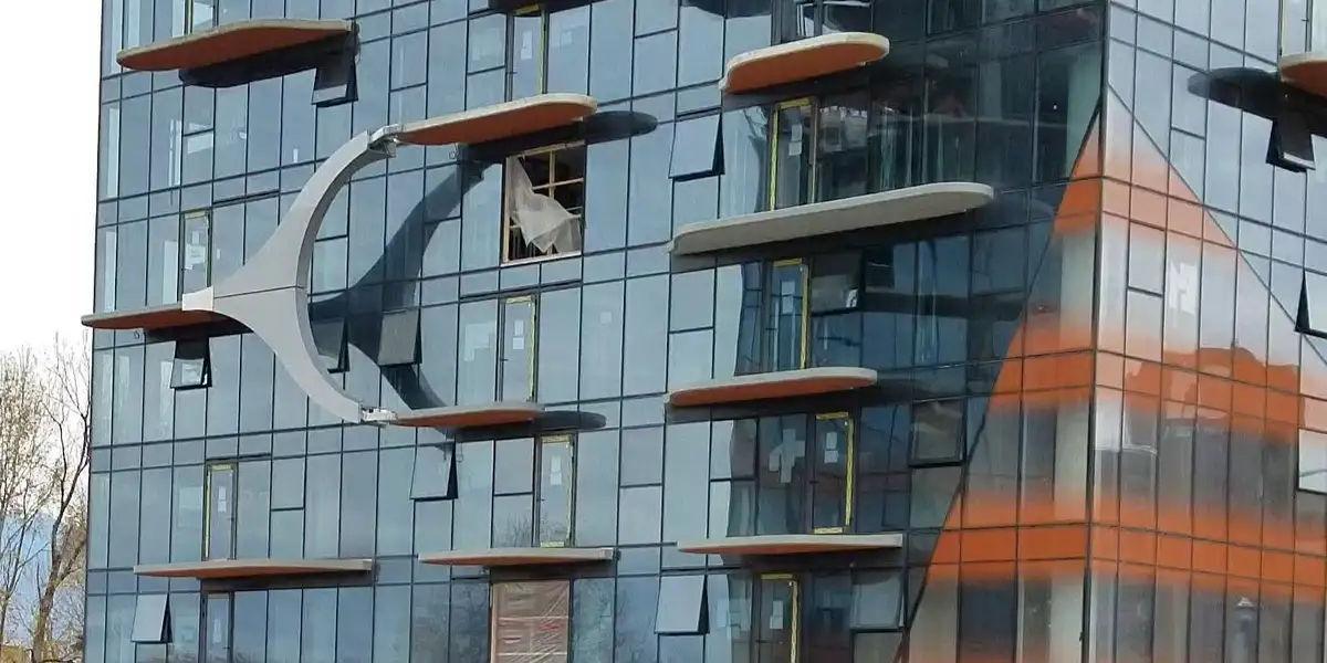 a modern glass building with unique, curved, floating balcony-like structures that resemble a spaceship's wing or engine…
