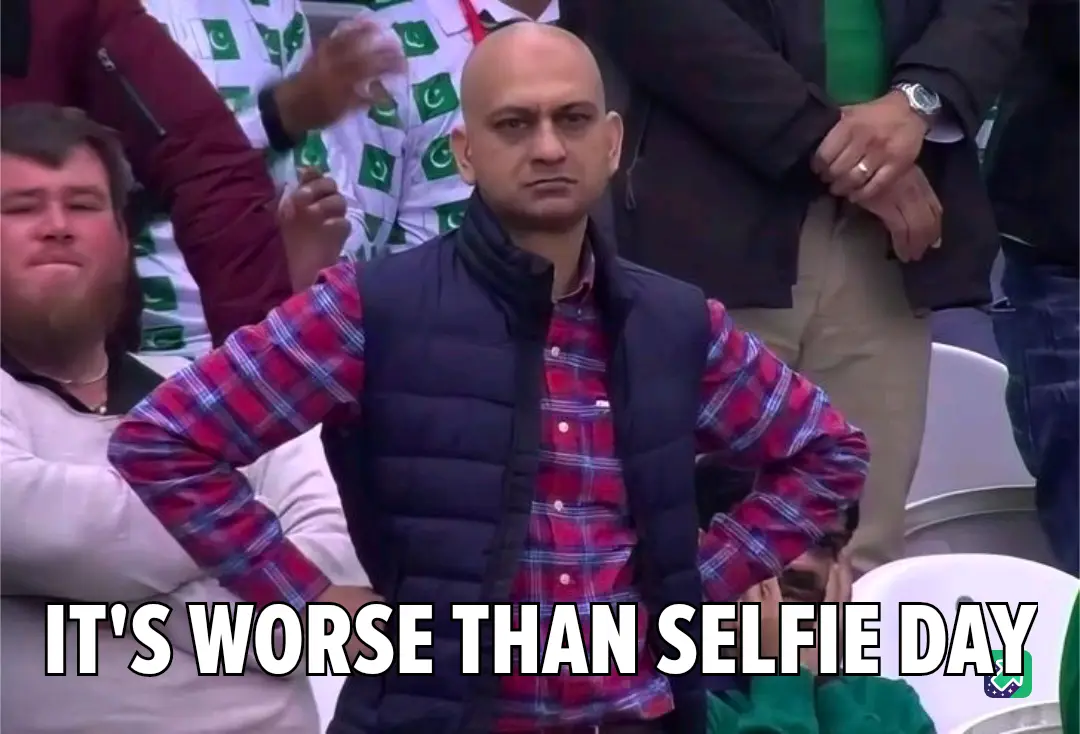 A bald man in a red plaid shirt and black vest stands with hands on hips in a stadium, looking intensely displeased. Behind…