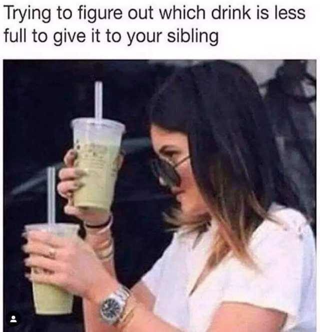 A woman with dark hair and sunglasses holds two identical plastic cups with straws, tilting them to compare their liquid…