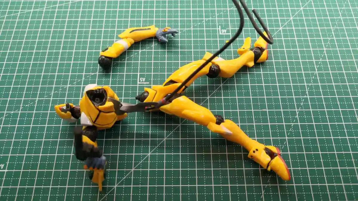 A yellow and black robot toy, resembling Bumblebee from Transformers, is shown disassembled and lying on a green cutting mat…