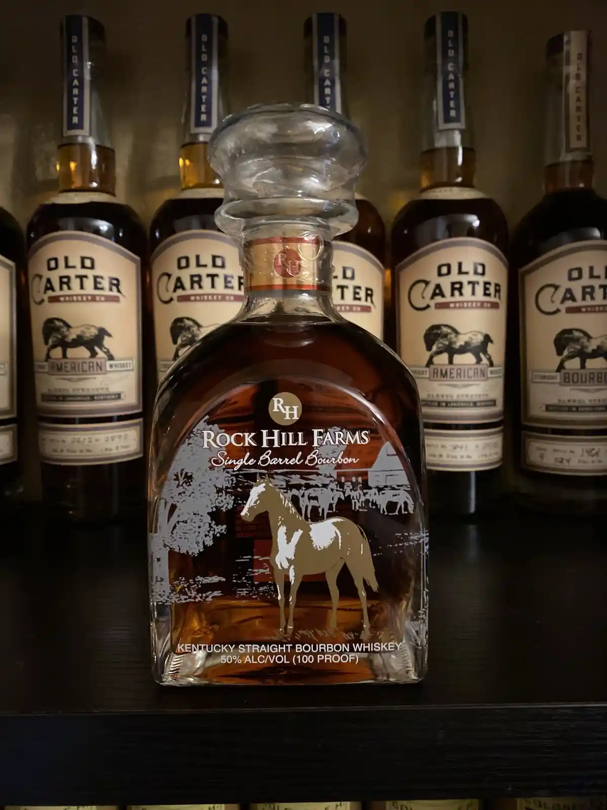 A bottle of Rock Hill Farms Single Barrel Bourbon whiskey with a horse illustration is prominently displayed on a shelf…
