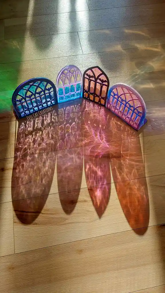 Four decorative, arched, stained-glass-style window cutouts with bat silhouettes are arranged on a wooden floor, casting…