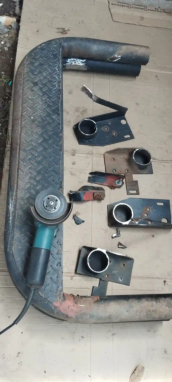 A top-down photo shows a large, curved metal pipe with a diamond plate texture, lying on cardboard. Resting on the pipe is a…
