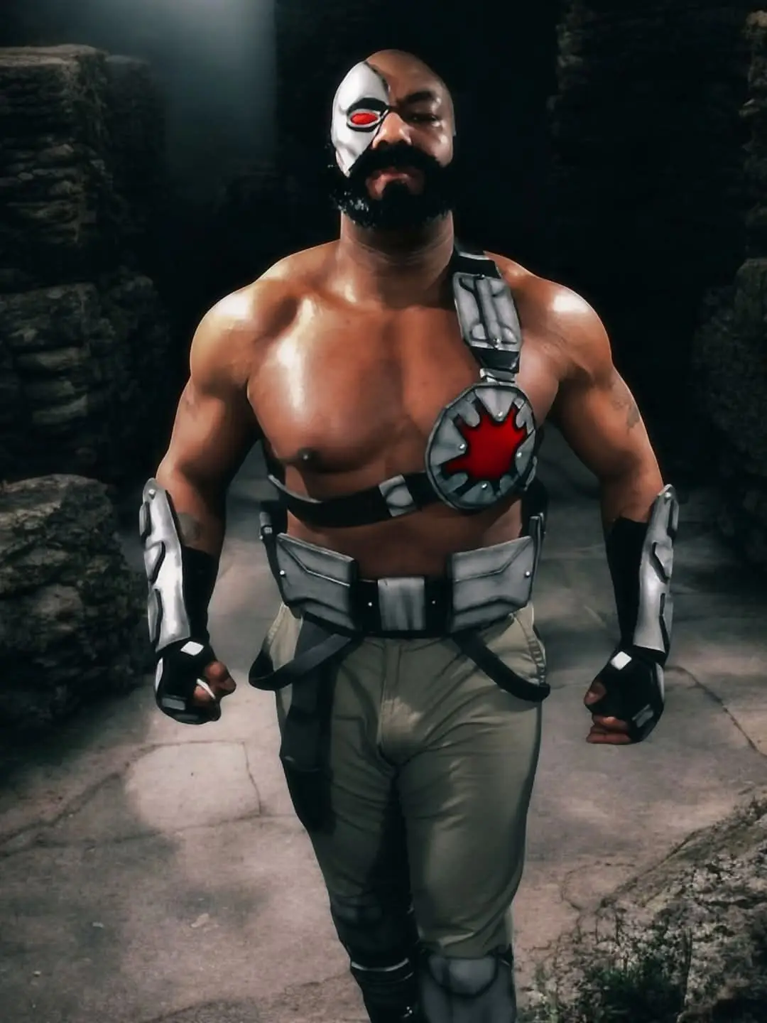 A muscular man with a black beard and a white-and-red half-mask resembling Batman's iconic design stands in a dimly lit…